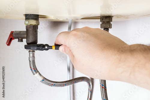 plumber hand fixes valve by adjustable wrench on boiler at home