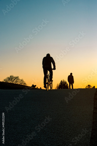 Man riding a bike on the hill during a sunset and also other people walking around