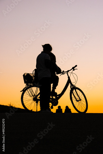 Woman with a bike during a sunset looking at other two people walking away