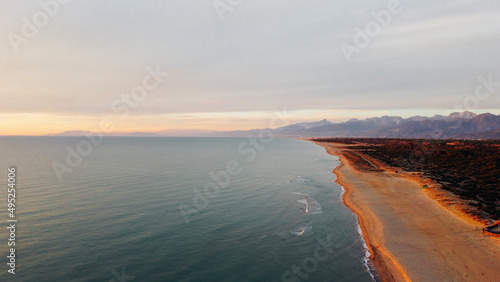 Aerial view of Ligurian sea, sandy shore and The Apuan Alps mountain range at sunset. Beautiful light and airy bird's eye view landscape in Tuscany region, Italy. Drone photography.