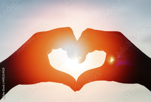 Love romance background concept. Hand heart shape with sunset sky with lover silhouette on the beach for Valentine day or summer vacation. photo