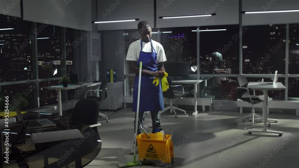 African-American janitor in uniform look at camera and smile in dark empty office downtown African-American janitor in uniform look at camera and smile in dark empty office downtown