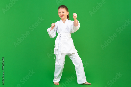 A child in a kimono on a green background. The girl fighter shows different techniques. © Юлия Дьякова