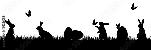 Cute Easter bunnies are playing on the grass. Butterflies fly, eggs lie in the grass. Silhouette