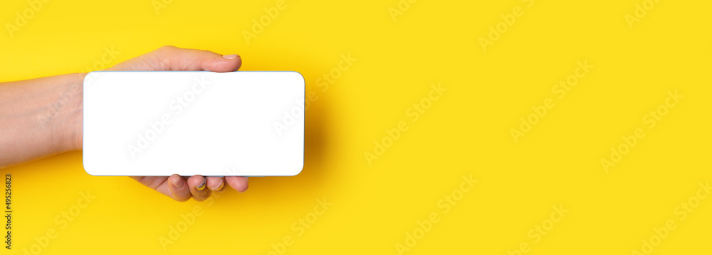 Obraz premium hand holding smartphone with white screen over yellow background, panoramic layout