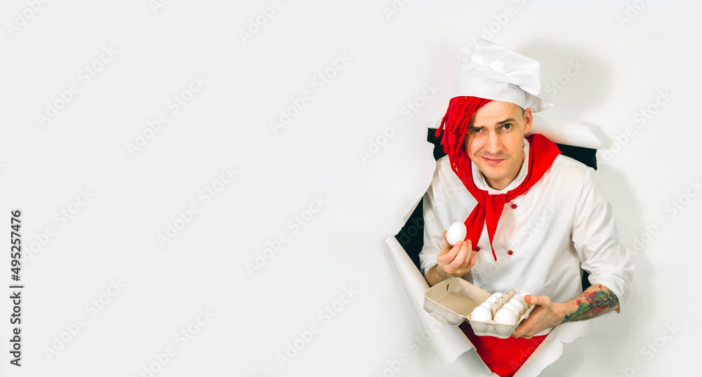 A handsome man with red dreadlocks holds it in his hand chicken eggs. Confident young cook in white shirt and red tie holding chicken eggs, peeking through ripped white paper background in studio A handsome man with red dreadlocks holds it in his hand chicken eggs. Confident young cook in white shirt and red tie holding chicken eggs, peeking through ripped white paper background in studio
