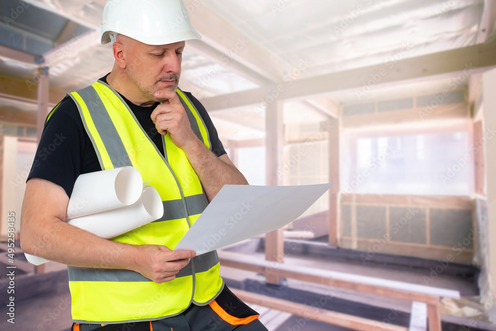Builder on a construction site. An architect with drawings in his hands. Civil engineer inside a house under construction. Man in a white helmet and a reflective vest. Construction professions. Builder on a construction site. An architect with drawings in his hands. Civil engineer inside a house under construction. Man in a white helmet and a reflective vest. Construction professions.