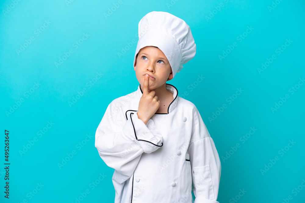 Little chef boy isolated on blue background having doubts while looking up Little chef boy isolated on blue background having doubts while looking up