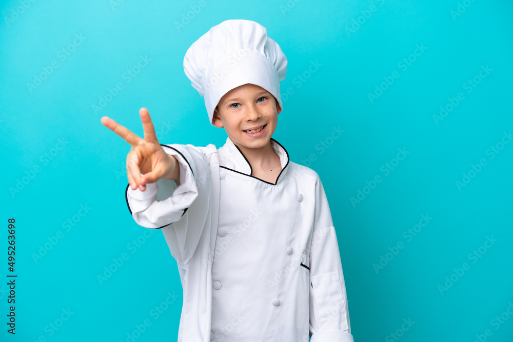 Little chef boy isolated on blue background smiling and showing victory sign Little chef boy isolated on blue background smiling and showing victory sign