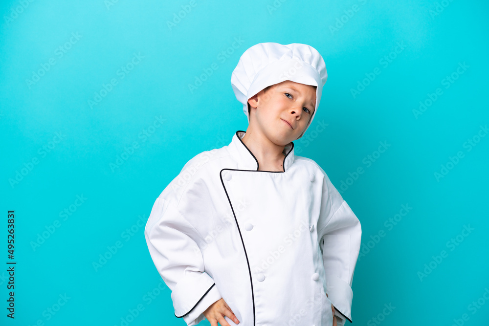Little chef boy isolated on blue background suffering from backache for having made an effort Little chef boy isolated on blue background suffering from backache for having made an effort
