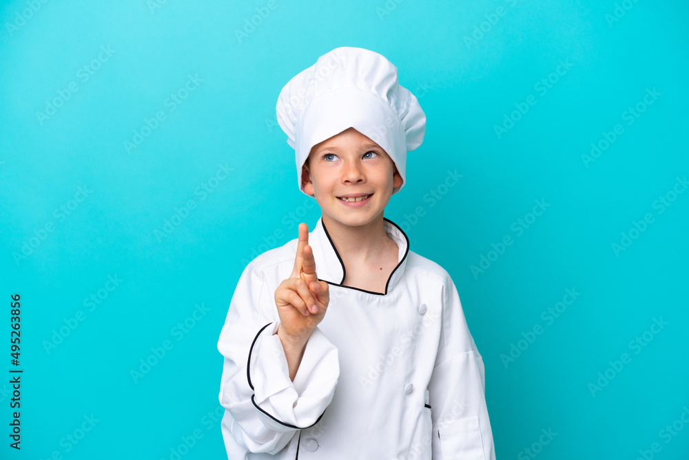 Little chef boy isolated on blue background with fingers crossing and wishing the best Little chef boy isolated on blue background with fingers crossing and wishing the best