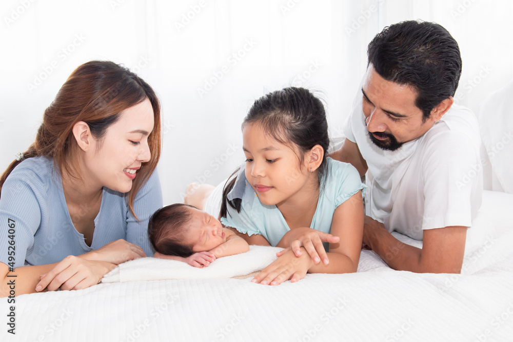 Asian parents and newborn with sister spend time together in bedroom. Adorable infant sleeping among happy family, mother and father lying in bed with two daughters.