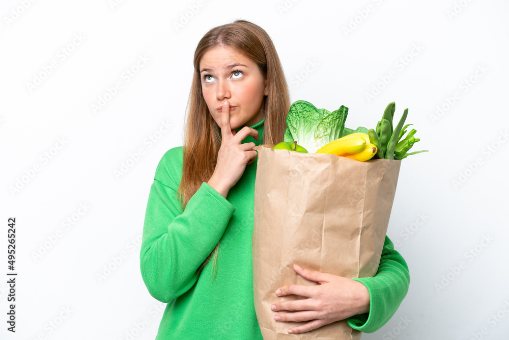 Young caucasian woman holding a grocery shopping bag isolated on white background having doubts while looking up Young caucasian woman holding a grocery shopping bag isolated on white background having doubts while looking up