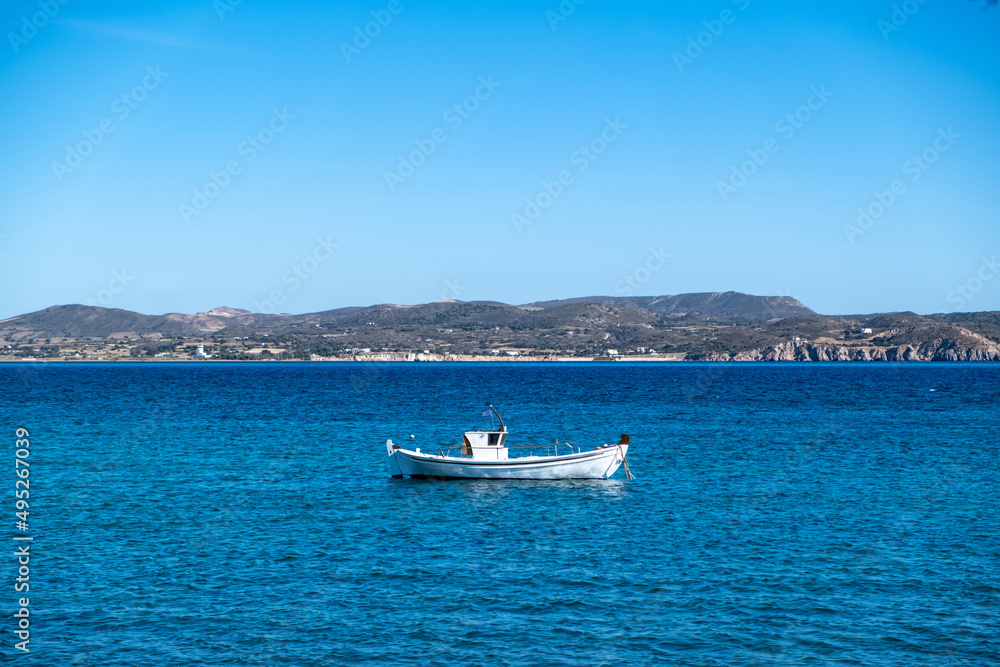 Milos Greek island, Cyclades. Fishing boat moored in open Aegean calm sea, blue sky background.