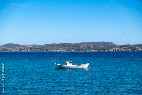 Milos Greek island, Cyclades. Fishing boat moored in open Aegean calm sea, blue sky background.