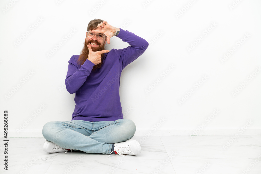 Young caucasian reddish man sitting on the floor isolated on white background focusing face. Framing symbol Young caucasian reddish man sitting on the floor isolated on white background focusing face. Framing symbol