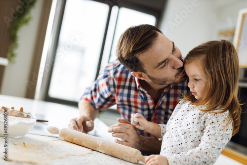 Father and his daughter using rolling pin on a dough and making cookies in the kitchen