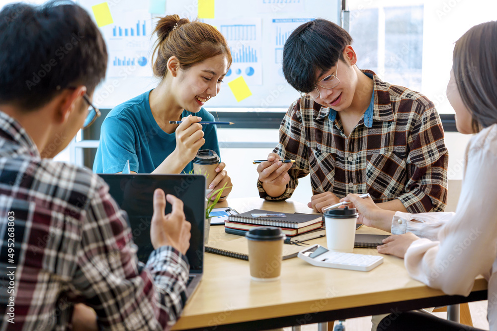 Four Asian coworkers startup discussing and smiling while sitting at the office.