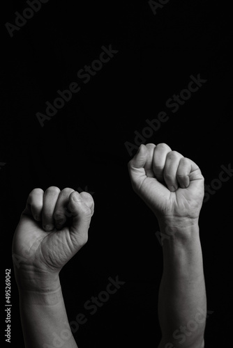 Vertical black and white image of two arms with clenched fists coming out from below. Close shot of a woman's and a man's arm with their fingers closed together leaving copy space.