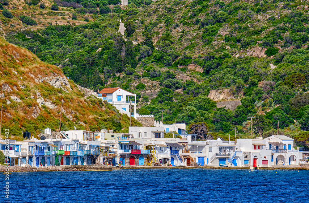 Village of Klima, Milos island, Greece on sunny summer day. Colorful fisherman houses by waterfront, high green hills in background