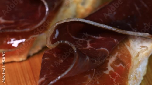 Slices of dried or smoked beef meat on slices o bread, macro shot close up view in 4k. Traditional spanish pinchos  rotating on wooden board.