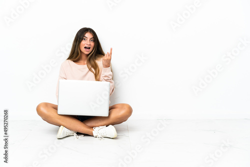 Young woman with a laptop sitting on the floor isolated on white background thinking an idea pointing the finger up