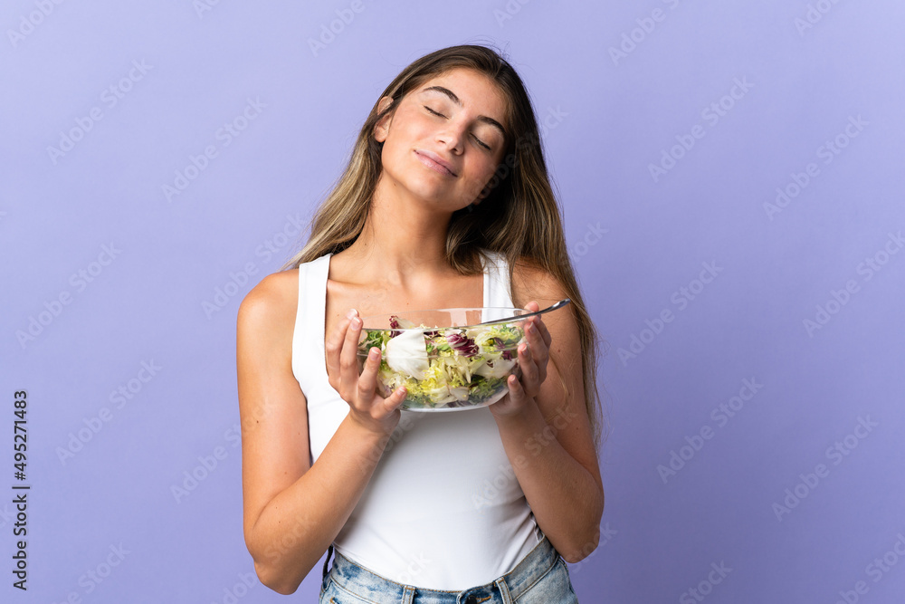 Young caucasian woman isolated on purple background holding a bowl of salad with happy expression