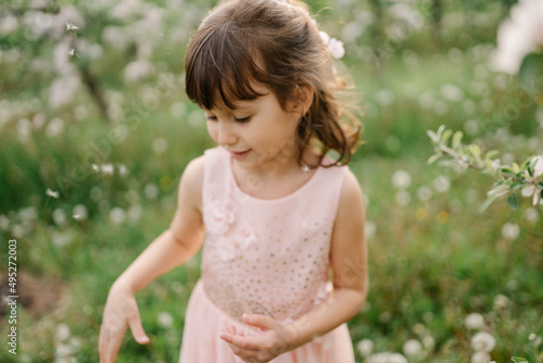 Portrait of little girl wearing light pink dress among blooming apple trees, white flowers in hair. Living in harmony with nature concept