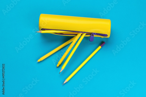 Yellow pencil case with yellow pencils and pens on a blue background. Flat lay.