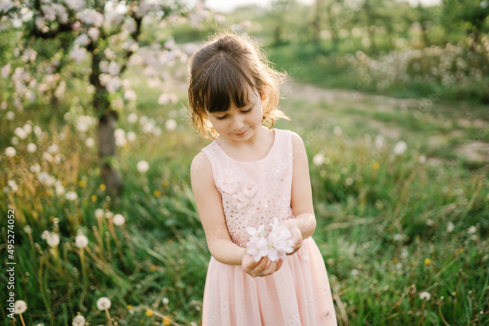 Little girl wearing light pink dress among blooming apple trees, white flowers in hair. Living in harmony with nature concept