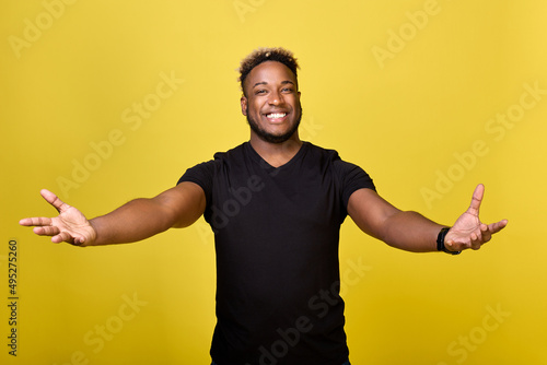 A swarthy guy of an athletic build has spread his arms in greeting, ready to hug you. An African-American man with a smile on his face stretched out his arms to meet his friend with open arms.