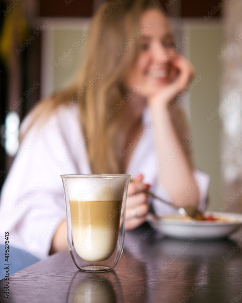Woman eating her breakfast and drinking coffee while sitting at the table. Focus on the latte Woman eating her breakfast and drinking coffee while sitting at the table. Focus on the latte