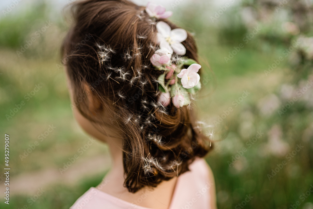 Little girl wearing light pink dress among blooming apple trees, white flowers in hair, french plait hairstyle. Living in harmony with nature concept Little girl wearing light pink dress among blooming apple trees, white flowers in hair, french plait hairstyle. Living in harmony with nature concept