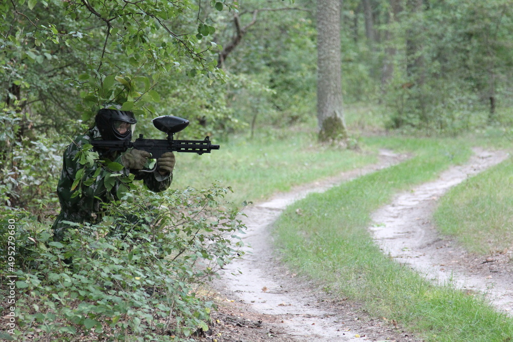 paintball sport player in protective uniform and mask aiming and shooting with gun outdoors of Forest