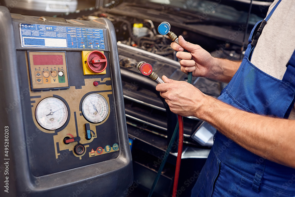 Mechanic holds a set of highpressure pipes for filling the car's air conditioning system. A/C