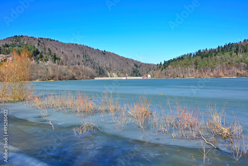 Klimkowka lake, hidden among the wild ranges of the Low Beskids, was created within the construction
 of a dam on the Ropa river, Poland. Frozen lake on a sunny early spring day photo
