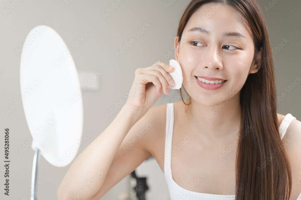 Happy asian woman looking at mirror and using cotton pad clean make up on her face Happy asian woman looking at mirror and using cotton pad clean make up on her face