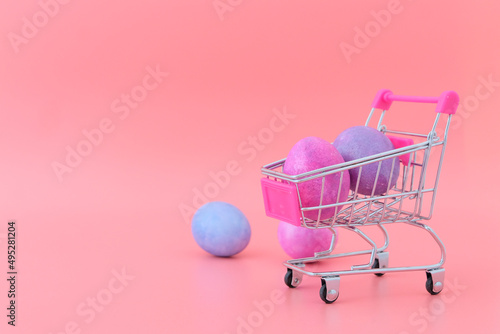 Eggs in lilac, purple, blue, pink colors in a grocery metal cart on a pink background. Easter concept in April. Festive decor, postcard.