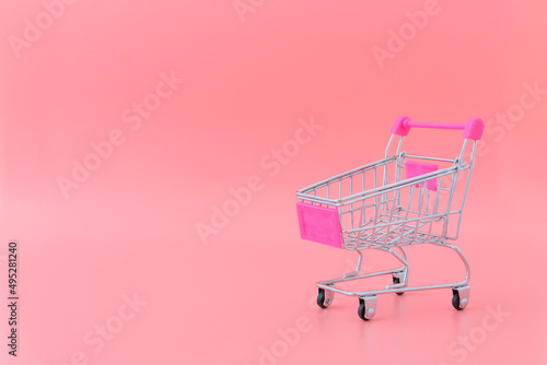 One metal grocery cart stands on a pink background. Women shopping concept.