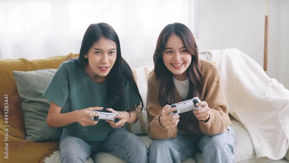 Happy young asian people playing video games and using Controllers while sitting on sofa in front of tv, Two Millennial spending fun time together at home. Happy young asian people playing video games and using Controllers while sitting on sofa in front of tv, Two Millennial spending fun time together at home.