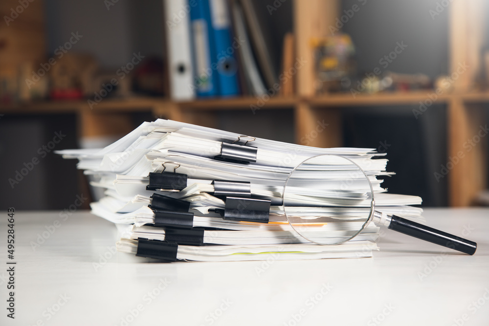 Stack of report paper documents with magnifying glass Stack of report paper documents with magnifying glass