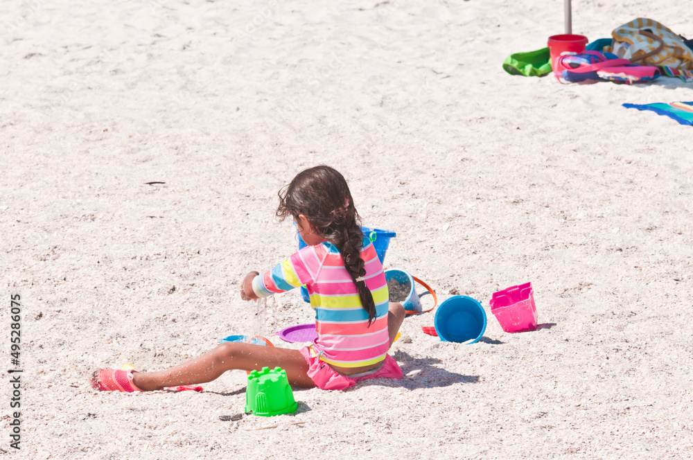back view, medium distance, of a little girl in a colorful bathing suit, playing with colored, plastic toys on a sunny, sandy, tropical, beach back view, medium distance, of a little girl in a colorful bathing suit, playing with colored, plastic toys on a sunny, sandy, tropical, beach