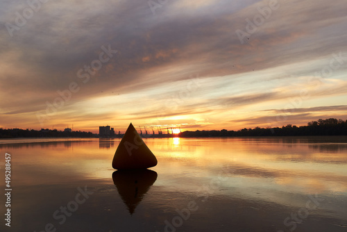 Inflatable triangular yellow buoy at sunrise on quiet water surface of autumn Danube river