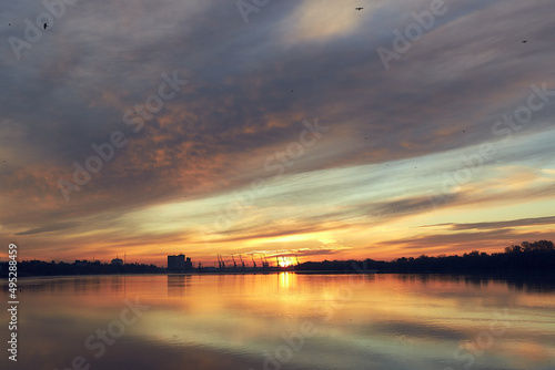 River at sunrise. Dramatic sky, glowing red clouds. Port terminal in the background. Concept winter landscape