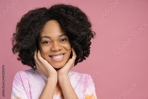 Beautiful smiling African American woman touching his face looking at camera isolated on pink background. Natural beauty 