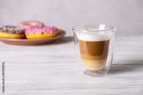 Glazed decorated donuts on plates and coffee latte or cappuccino with milk foam in a heat-resistant glass cup. Selective focus.