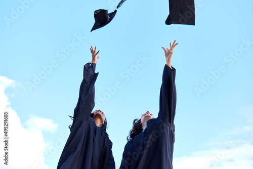 The famous graduation day tradition. Low angle shot of two attractive young female students celebrating on graduation day.
