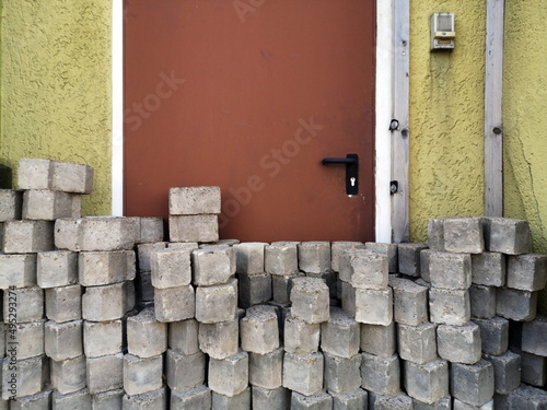 Gestapelte graue Pflastersteine auf dem Bürgersteig vor einer braunen Stahltür einer alten Werkstatt in Oerlinghausen bei Bielefeld am Hermannsweg im Teutoburger Wald in Ostwestfalen-Lippe