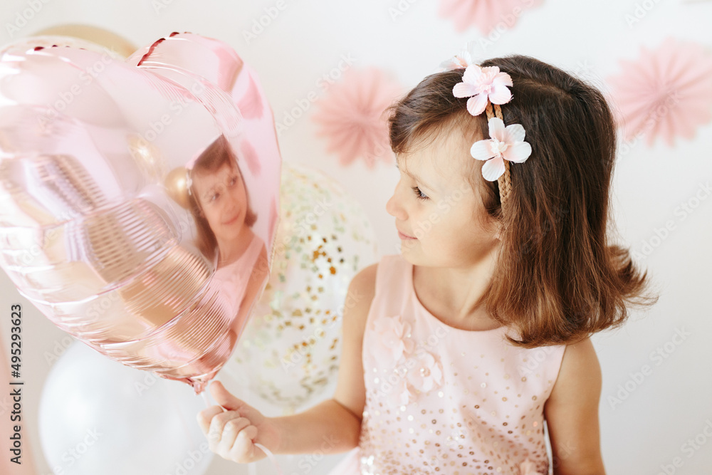 Six year girl wearing dress holding light pink heart shaped balloon. Home birthday party Six year girl wearing dress holding light pink heart shaped balloon. Home birthday party