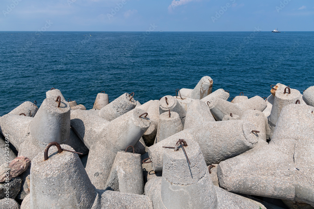 Large tetrapod concrete blocks lies on breakwater by blue sea water in a sunny day. Calm water. Coastal management theme. Large tetrapod concrete blocks lies on breakwater by blue sea water in a sunny day. Calm water. Coastal management theme.
